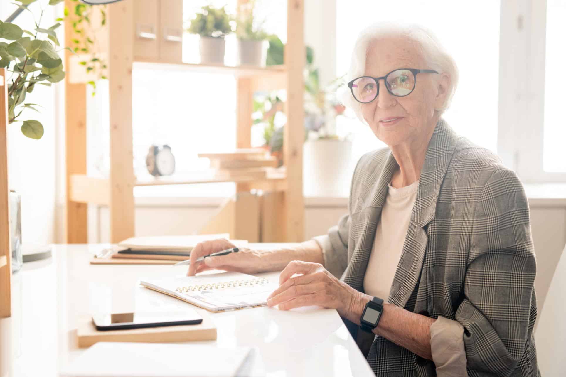 Dona gran amb ulleres escrivint o planificant el seu testament en una oficina lluminosa
