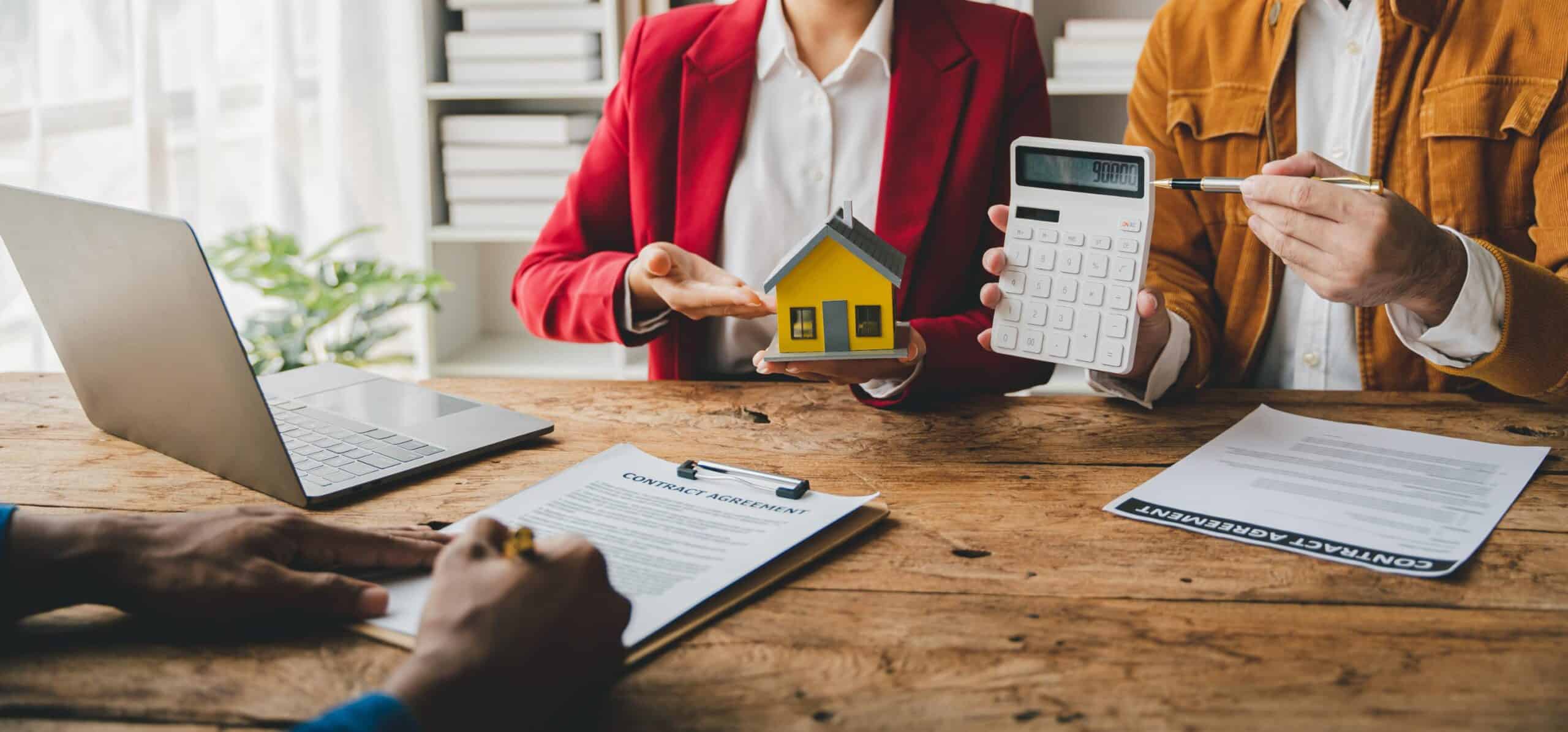 Agents immobiliaris mostrant una maqueta de casa i càlculs amb una calculadora, representant el servei de valoració gratuïta d’un immoble.